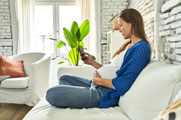 Pregnant, content Caucasian woman on sofa, phone in hand.