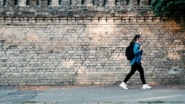 a woman tourist with a backpack walks down the street past a brick wall.
