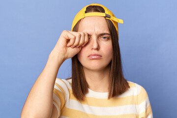 Unhappy sad upset teenager girl wearing striped t-shirt and baseball cap standing isolated over...