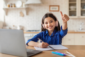 Schoolgirl At Laptop Learning And Gesturing Thumbs Up At Home