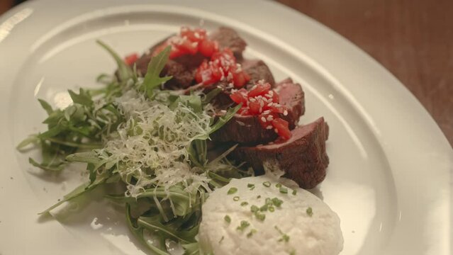 No people closeup of medium beef steak with arugula leaves on white plate in expensive restaurant