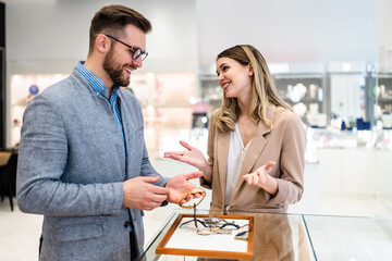 Elegant middle age businessman choosing and buying his new expensive watch. Beautiful young female...