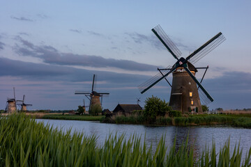 Fototapeta na wymiar Beautiful wooden windmills at sunset in the Dutch village of Kinderdijk. Windmills run on the wind. The beautiful Dutch canals are filled with water. Beautiful sunset.