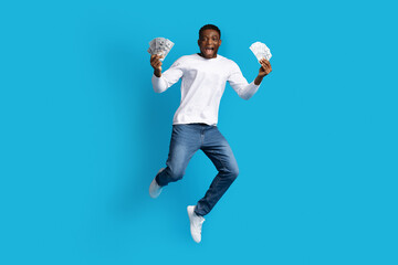 Fototapeta na wymiar Black guy jumping with money cash in hands, blue background