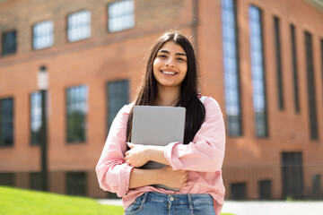 Portrait of happy hispanic lady student posing with laptop in hands outdoors, looking and smiling...