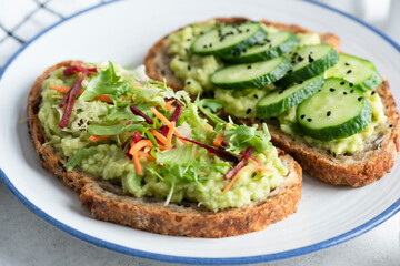 Avocado toast with different healthy vegan toppings. Cucumber, mixed greens, grated beet and carrot with seeds and olive oil. Healthy food