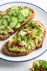 Avocado toast with different healthy vegan toppings. Cucumber, mixed greens, grated beet and carrot with seeds and olive oil. Healthy food
