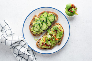 Vegan avocado toasts with toppings of cucumber and fresh green salad with grated carrot and raw beet. Clean eating, dieting concept. Top view
