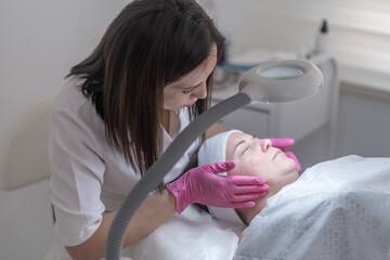 The beautician uses a magnifying lamp to examine the client's skin and cure any skin problems...