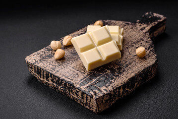 Delicious sweet white chocolate broken into cubes on a wooden cutting board