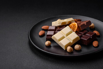 A mix of several types of delicious sweet chocolate broken into cubes on a black plate