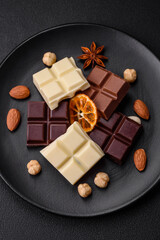 A mix of several types of delicious sweet chocolate broken into cubes on a black plate