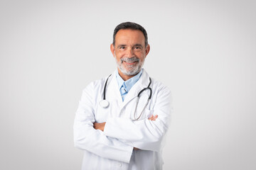 Cheerful confident caucasian mature man doctor in white coat with crossed arms on chest looks at...