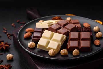 A mix of several types of delicious sweet chocolate broken into cubes on a black plate