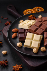 A mix of several types of delicious sweet chocolate broken into cubes on a black plate