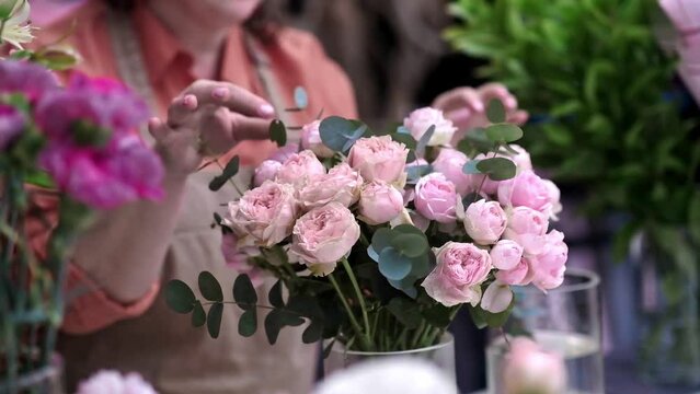 Expert flower decorator using her hands to create a beautiful bouquet of pink roses up close. slower shop