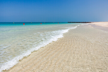 Fototapeta na wymiar Sandy beach on coast with crystal clear water in sea, red buoys