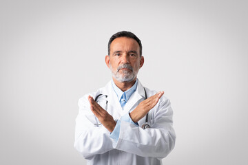 Sad serious confident caucasian mature man doctor in white coat crossed his arms, make stop gesture