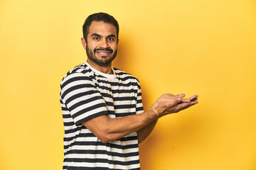 Casual young Latino man against a vibrant yellow studio background, holding a copy space on a palm.