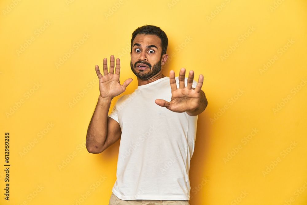 Wall mural Casual young Latino man against a vibrant yellow studio background, being shocked due to an imminent danger