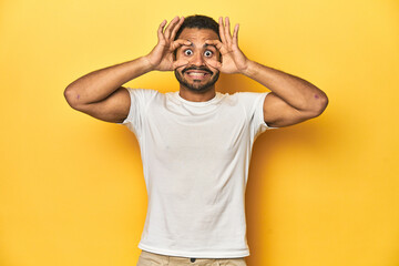 Fototapeta na wymiar Casual young Latino man against a vibrant yellow studio background, keeping eyes opened to find a success opportunity.