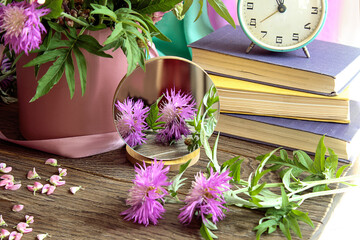 Summer bouquets: lilac cornflowers are reflected in the mirror against the background of a stack of books, close-up