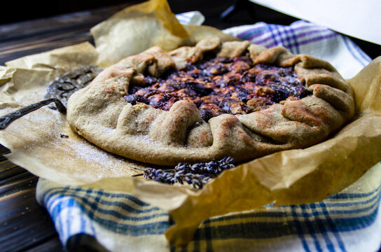  Sweet french homebaked galette with plums and cinnamon lying on semitransparent paper for baking and tablecloth decorated with dried lavender and vintage fork. Food photo for blog, magazine, recipe