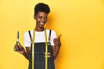 African tailor with scissors and measuring tape, fashion concept smiling and raising thumb up