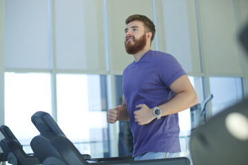 Happy young fit man training in the gym, running jogging on treadmill, doing cardio exercise and smile. Healthy lifestyle, sport, fitness concept