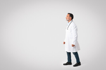 Serious caucasian mature man doctor in white coat look at copy space, isolated on gray background, studio
