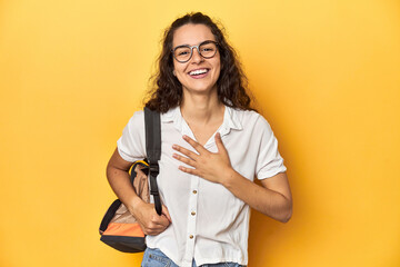 Caucasian university student with glasses, backpack, laughs out loudly keeping hand on chest.