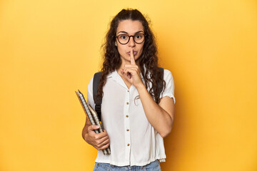 Student holding notebooks, glasses, backpack on, keeping a secret or asking for silence.
