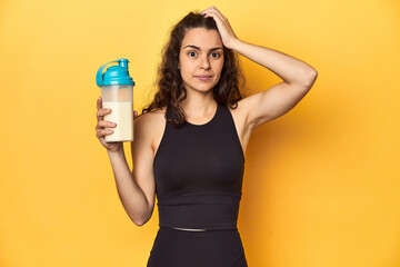 Woman holding a protein shake, in sportswear, being shocked, she has remembered important meeting.