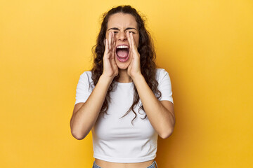 Young Caucasian woman, yellow studio background, shouting excited to front.