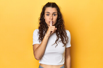 Young Caucasian woman, yellow studio background, keeping a secret or asking for silence.