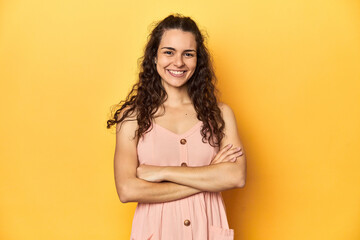 Young Caucasian woman, yellow studio background, who feels confident, crossing arms with determination.