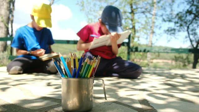 Two brothers study, draw, read in the backyard of the house on a sunny day. Concept of education, childhood, parenting, summer vacations, and studying.