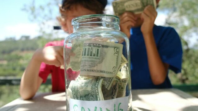 Money-Savvy Kids: Encouraging Financial Responsibility through Saving Habits. They carefully place both dollars and bitcoins into the jar, showcasing their financial awarenes