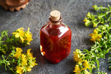 A bottle of St. John's wort oil with fresh flowers on a table