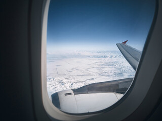 Flying over snow capped mountains. View of snowy landscape under the plane wing through plane...