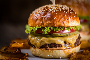 Tasty cheeseburger with lettuce, cheddar cheese, tomato and pickles. Burger bun with sesame seeds. Rustic atmosphere. Delicious fast food meal.