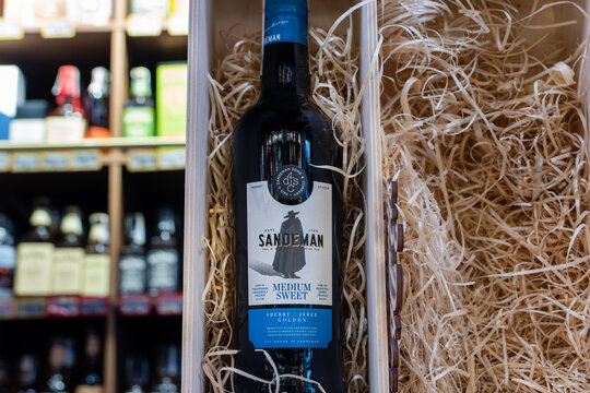 Bottle of Spain sherry wine Sandeman Medium Sweet close-up in wooden wine box with wood chips on blurred background of wine shelves. Ukraine, Zhytomyr, June, 12, 2023