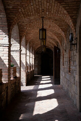 Sun light shinning through arched brick windows in a long castle corridor.