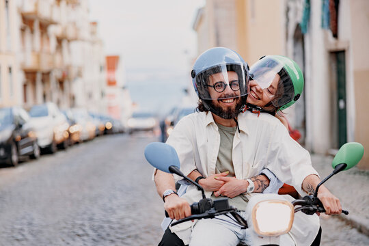 Happy young couple in protective hats are riding on vintage scooter in the Lisbon street