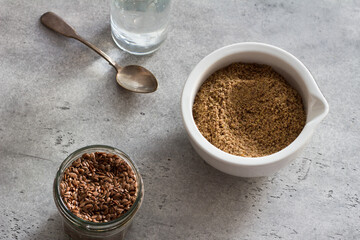 Flax seeds in a glass jar, ceramic a bowl of ground flax and water for soaking the flax and making healthy meals on a gray textured background