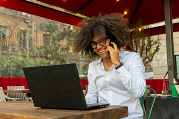 Energetic Afro Guy: Smiling and Engaged in Phone Call While Working on Laptop. Tech-Savvy...