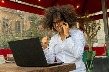 Energetic Afro Guy: Smiling and Engaged in Phone Call While Working on Laptop. Tech-Savvy...