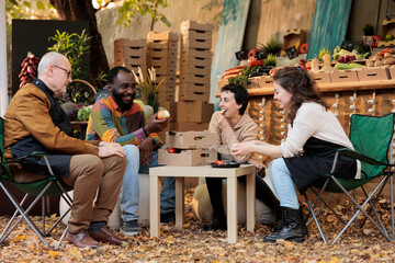 Happy young diverse couple tasting apples at farmers market on sunny autumn day. Friendly local vendors introducing no-spray eco fruits and vegetables to customers at local organic bio food fair