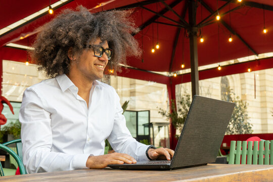 Energetic Afro Guy: Smiling and Engaged in Phone Call While Working on Laptop. Tech-Savvy Afro-Haired Guy: Dynamic Phone Conversation with Laptop Workstation. Productivity in Action.