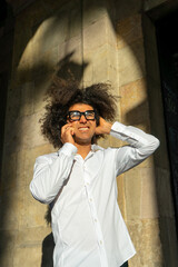 Stylish Urban Communication: Afro-Haired Guy in White Shirt and Glasses. City Charisma: Energetic Afro-Haired Guy Engaged in Phone Conversation. Dynamic Conversations: Afro Style in the Urban